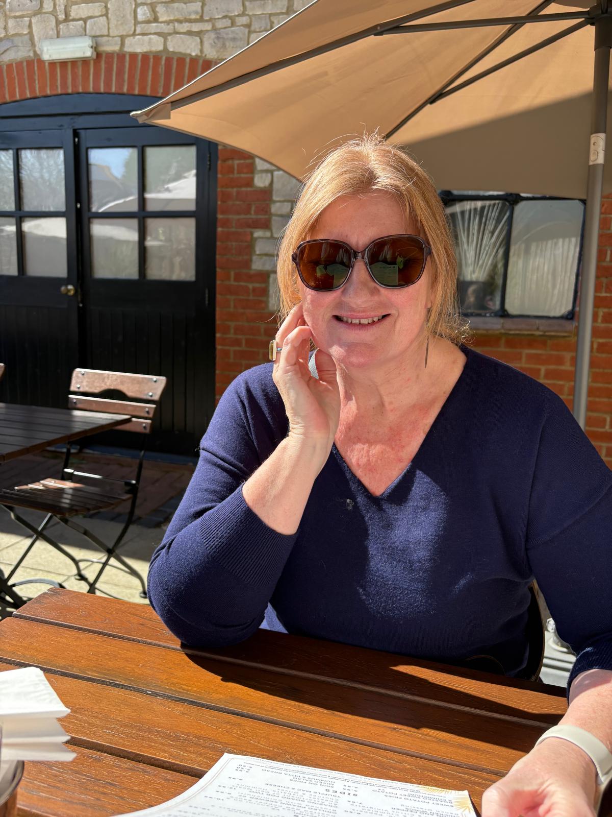 Claire, smiling, sitting at a table outdoors in the sunshine